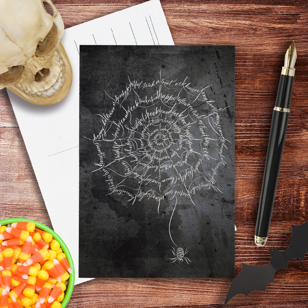 A top lifestyle view of the Halloween calligraphy postcard: "spider web" design