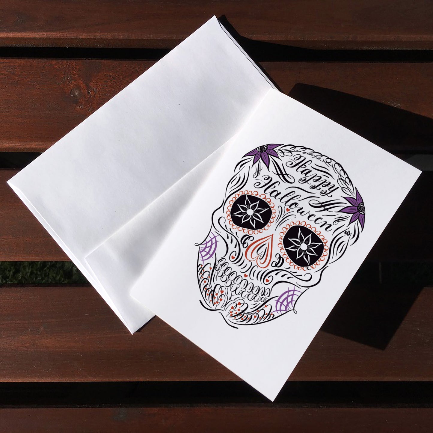 A top lifestyle view of the halloween calligraphy postcard: "Sugar Skull" design