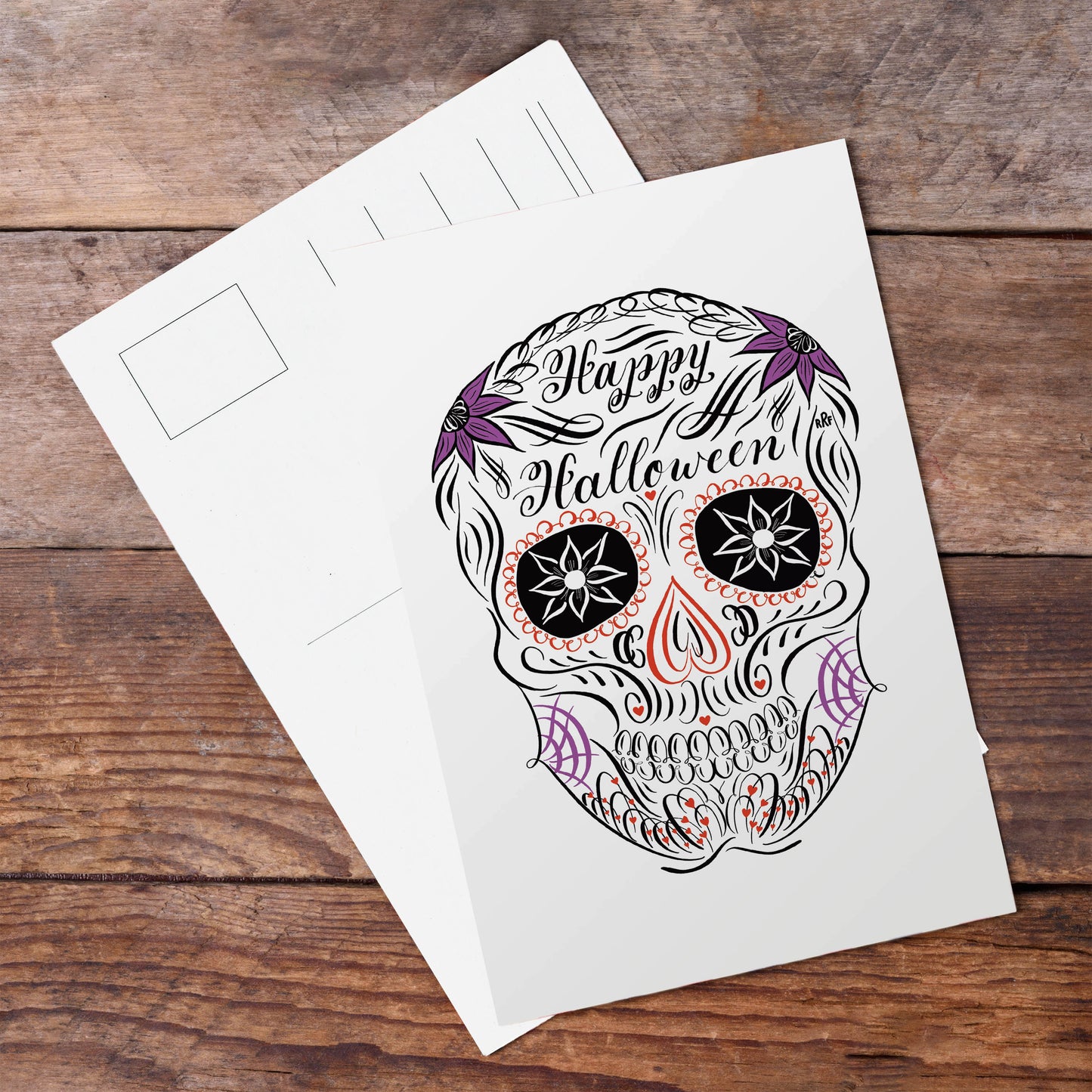 A lifestyle view of the halloween calligraphy postcard "sugar skull" design
